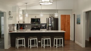 Une cuisine moderne dotée d’un îlot central, de tabourets de bar, d’appareils électroménagers en acier inoxydable et de luminaires suspendus.