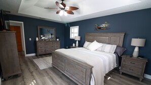 Une chambre à coucher avec un lit en bois, des tables de chevet, une commode, un ventilateur de plafond et un grand miroir.