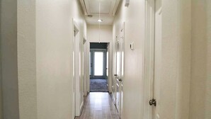 Un couloir étroit aux murs blancs et au plancher en bois, qui mène à une porte au fond.