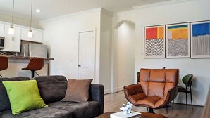 Un salon moderne avec un canapé, un fauteuil en cuir, une table basse et une cuisine en arrière-plan.