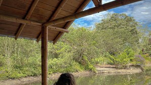 A person relaxing on a wooden deck with a view of a calm river and dense greenery. - HOSTERIA KUMBHA MELA (Mindo)