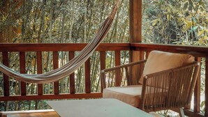 A hammock, a wicker chair, and a small table on a wooden deck with a view of bamboo trees. - HOSTERIA KUMBHA MELA (Mindo)