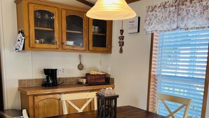 A dining area with a wooden table and chairs, a hanging light fixture, and a window with blinds.