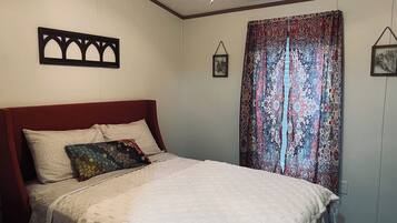 Une chambre à coucher avec un lit, une tête de lit, un rideau à motifs et un cadre photo fixé au mur.