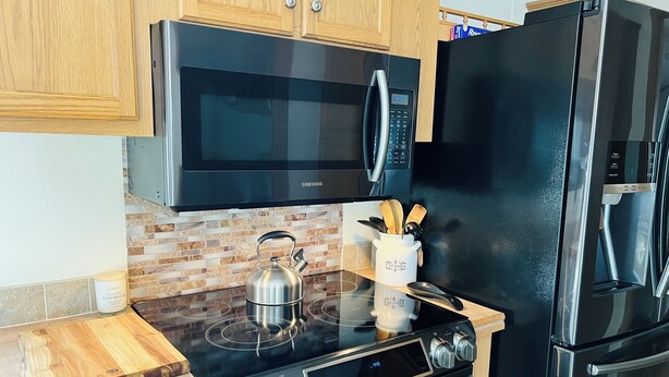 A modern kitchen with a stainless steel stove, black microwave, and refrigerator.