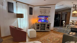 A living room with a sofa, ottoman, TV, and a dining area with chairs and a table.
