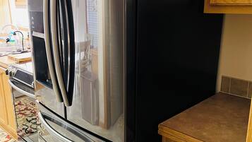 A stainless steel Samsung refrigerator with a freezer drawer, a built-in oven, and a wooden countertop drawer with utensils.