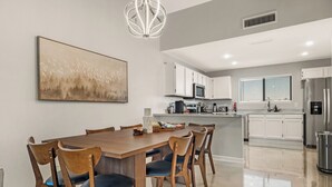 Una cocina moderna con armarios blancos, un refrigerador de acero inoxidable y una zona de comedor con mesa y sillas de madera.