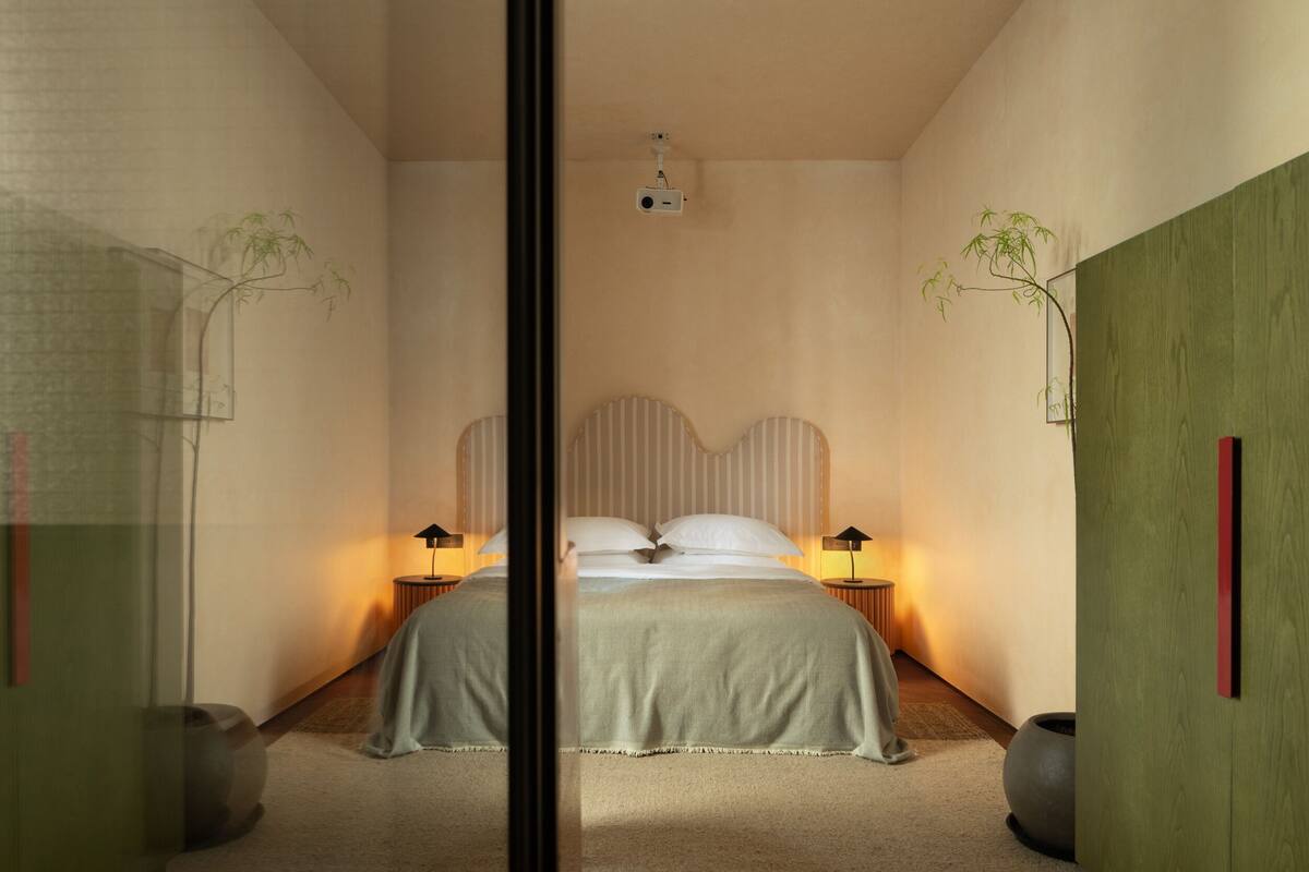 A bedroom with a large bed, two bedside tables with lamps, and a ceiling projector.