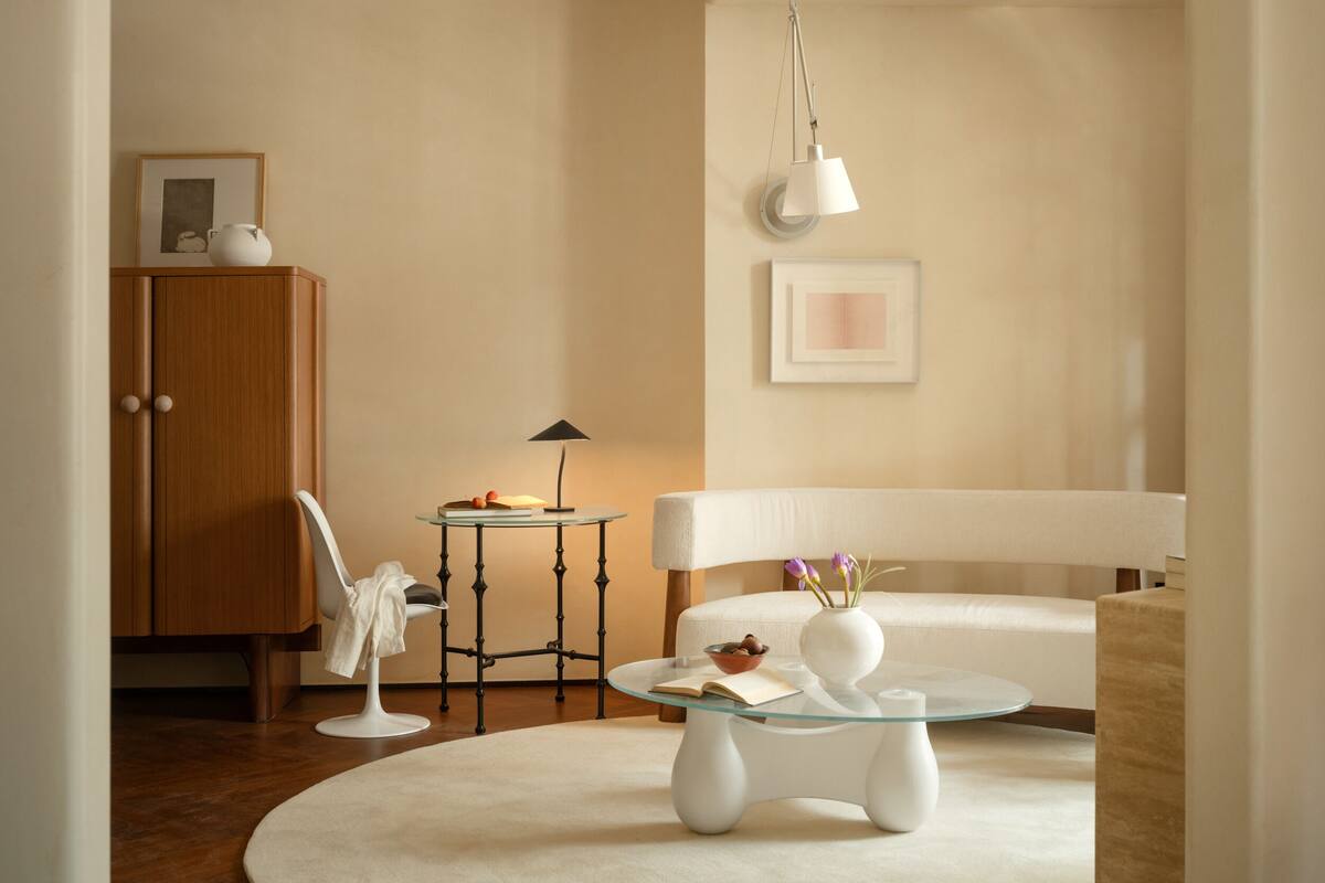 A modern living room with a round glass coffee table, a white sofa, a wooden cabinet, and a small round table with a lamp.
