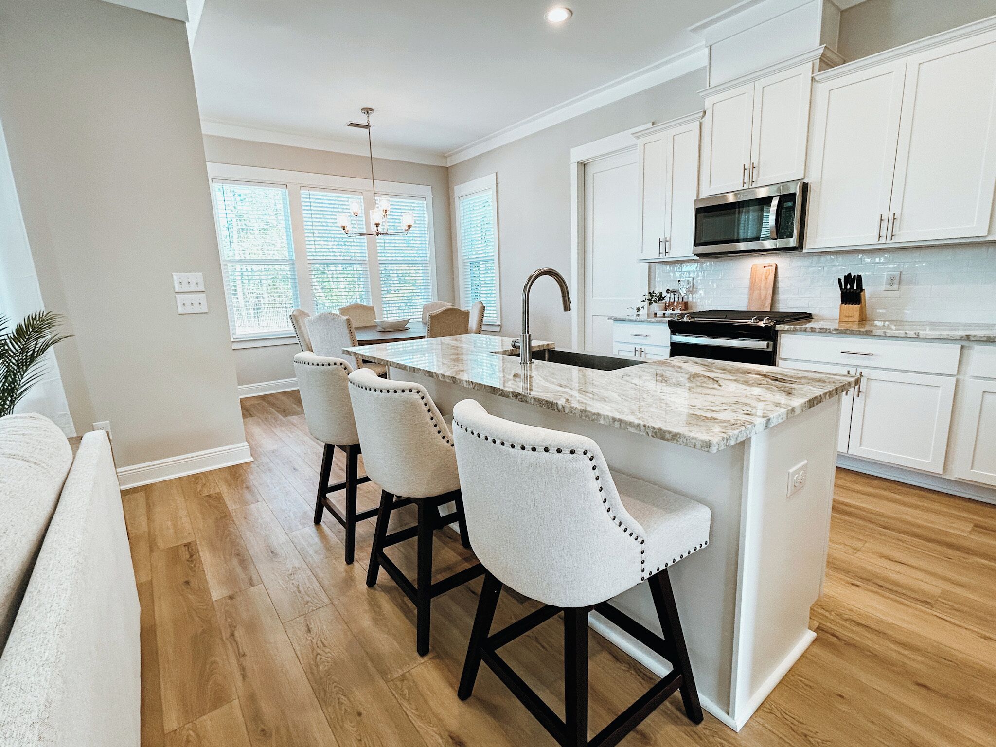 A modern kitchen with white cabinetry, a central island with bar stools, a built-in microwave, and a large window providing natural light.