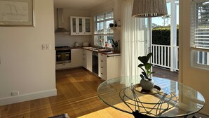 Une cuisine moderne avec des meubles blancs, une table à manger en verre et un luminaire suspendu.