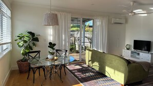Un salon moderne avec une table à manger en verre, un canapé vert et un téléviseur posé sur un meuble blanc.