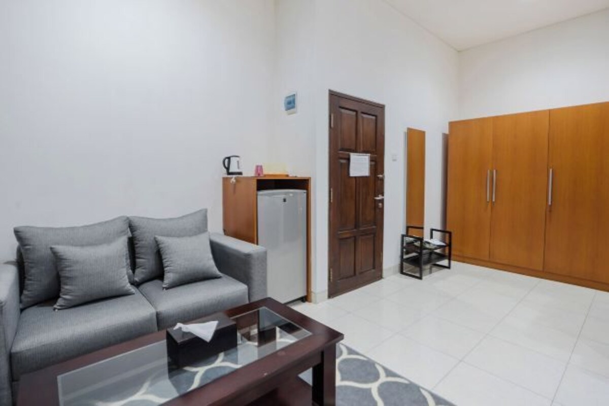A living room with a grey sofa, a glass coffee table, a wooden wardrobe, and a small cabinet.