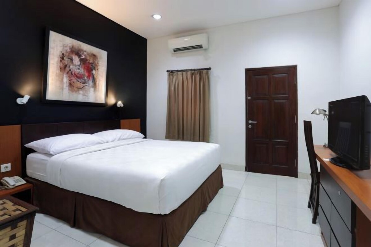 Une chambre d’hôtel comprenant un lit, une télévision, un bureau, une chaise, un appareil de climatisation, une porte et un tableau au mur.