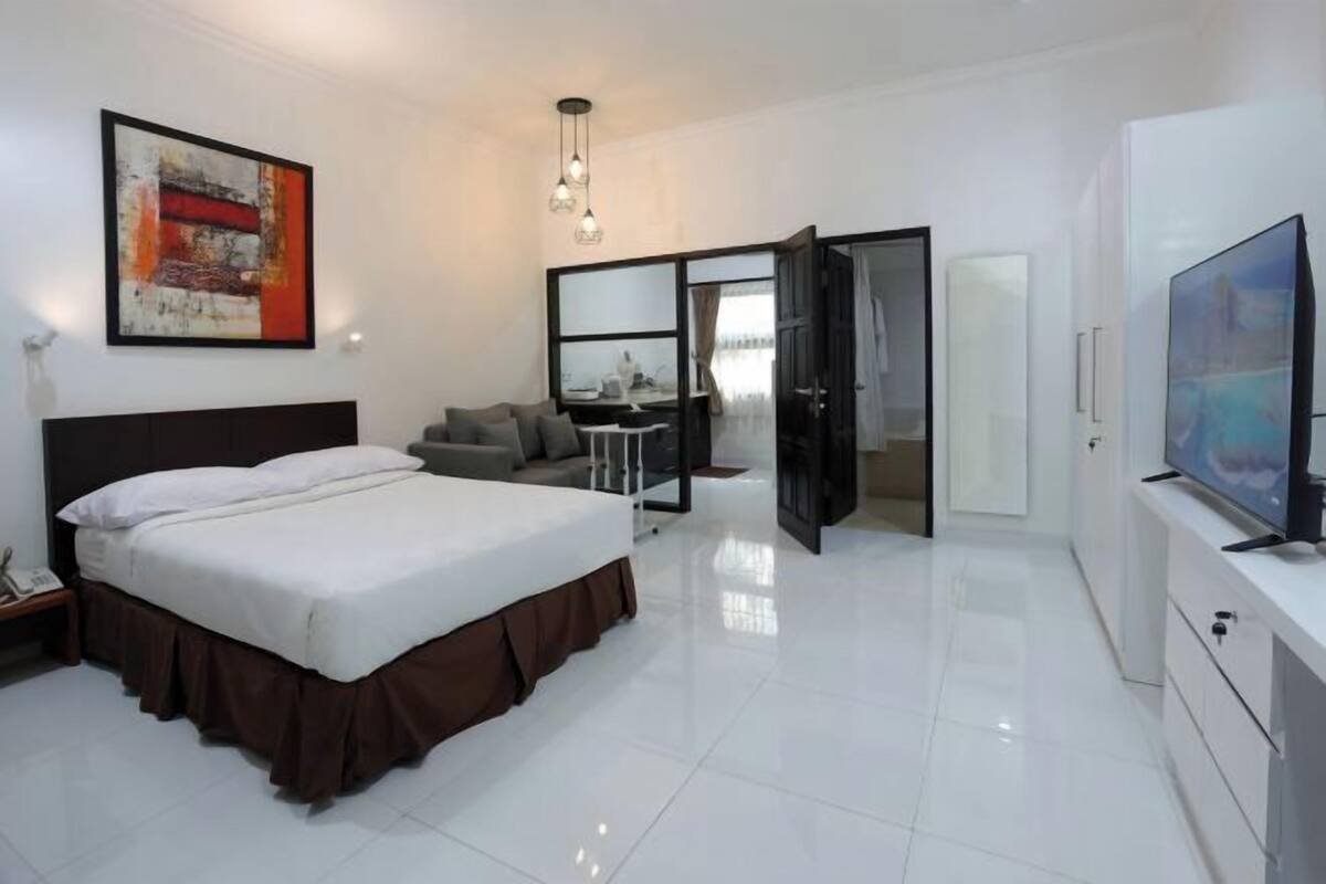 A modern hotel room with a large bed, a television, a desk, and a mirror.