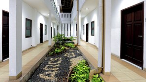 Un pasillo con jardín central, paredes blancas y puertas a ambos lados.