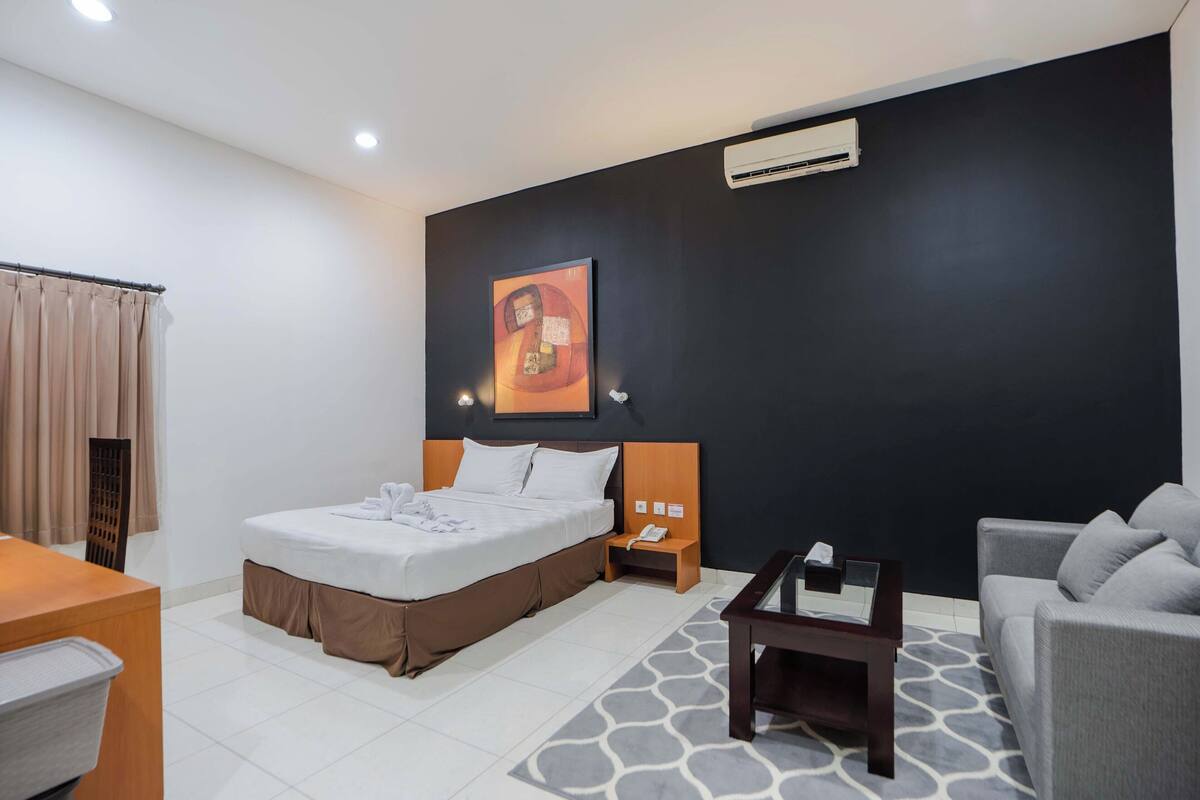 A hotel room with a bed, a desk, a sofa, a nightstand, and a painting on the wall.