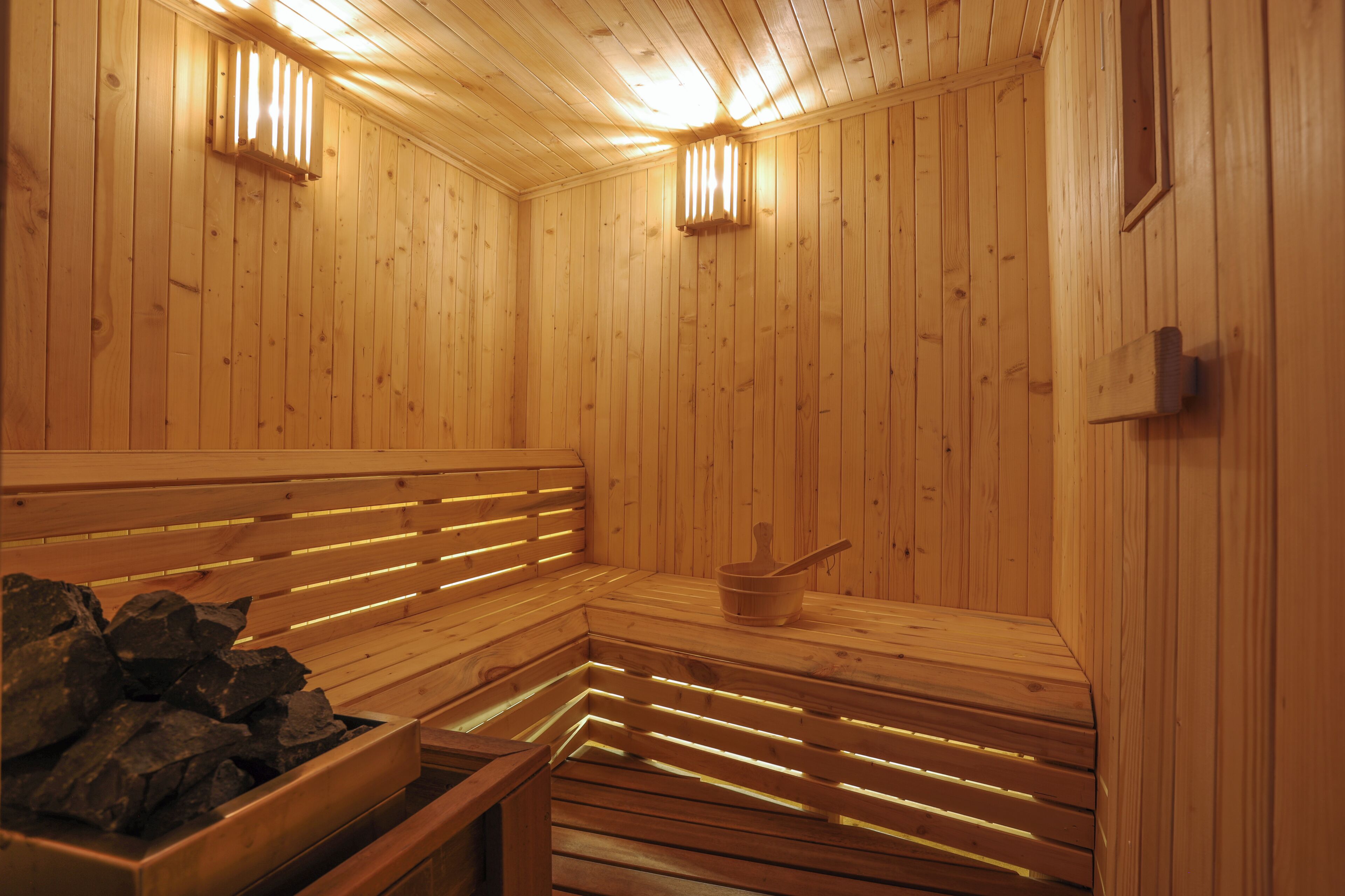 A sauna with wooden benches and benches, a bucket, and a stone-filled container.