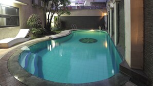 Una piscina con solárium empedrado, una tumbona y un pequeño árbol.