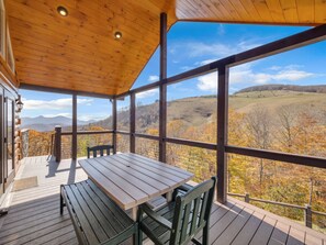A wooden deck with a table and chairs, overlooking a scenic landscape with hills and autumn foliage. - 6BR Mountain Lodge Hot Tub, Game Room, Groups (Banner Elk)