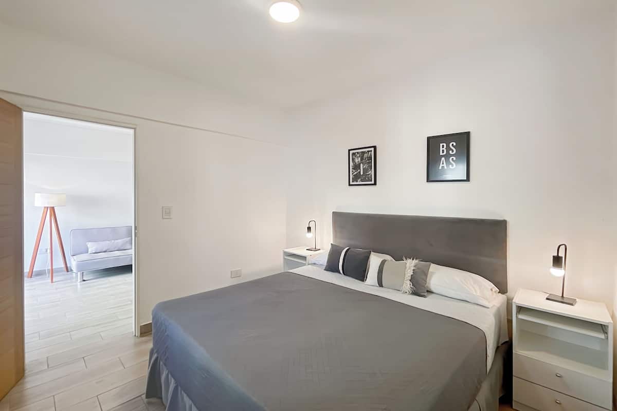 A modern bedroom with a large bed, bedside tables, and a view of a balcony.