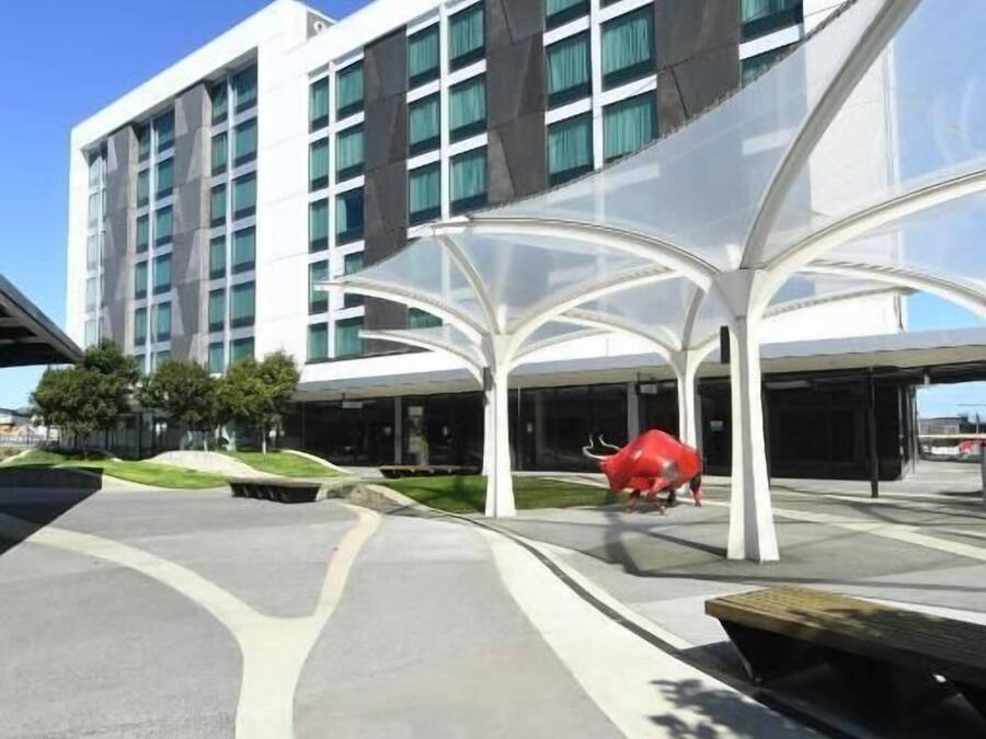 A modern building with a glass facade, a central red bull sculpture, and a covered walkway.