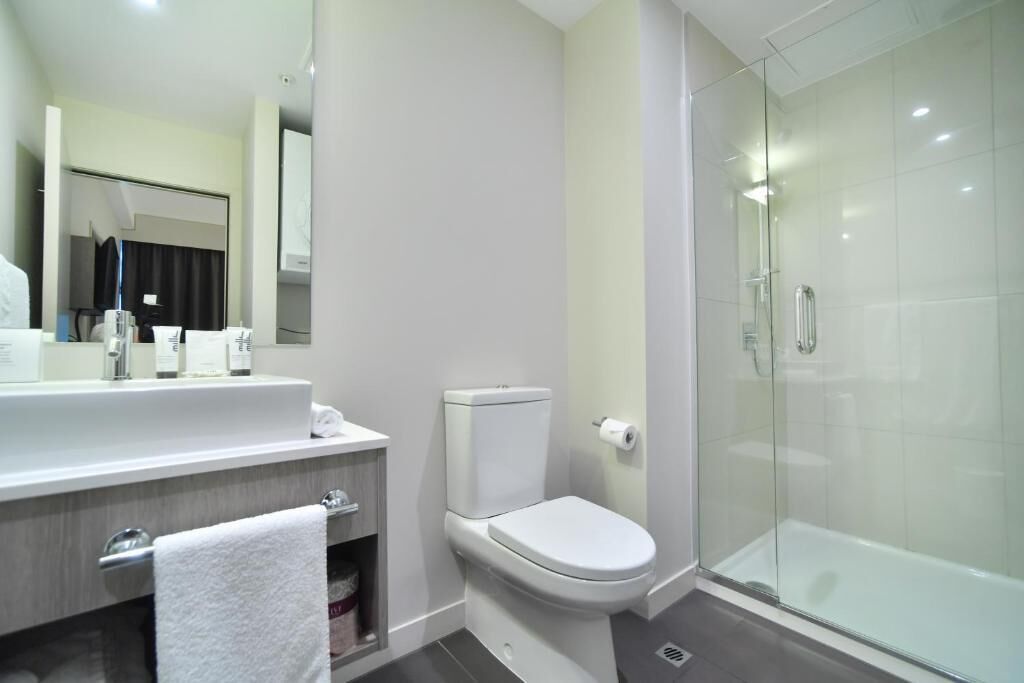 Une salle de bain moderne avec une douche à parois de verre, des toilettes blanches et un meuble-lavabo doté d’un miroir et d’articles de toilette.
