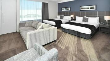 Een hotelkamer met twee bedden, een bank, een stoel, een groot raam en uitzicht op de stad.