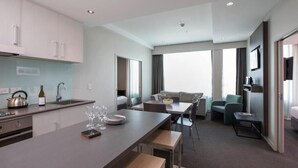 A modern hotel room with a kitchenette, a dining area, and a seating area with a sofa and chairs. - Quest Highbrook (Auckland)