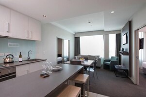 Quarto de hotel moderno com cozinha compacta, área de refeições e sala de estar com sofá e cadeiras.