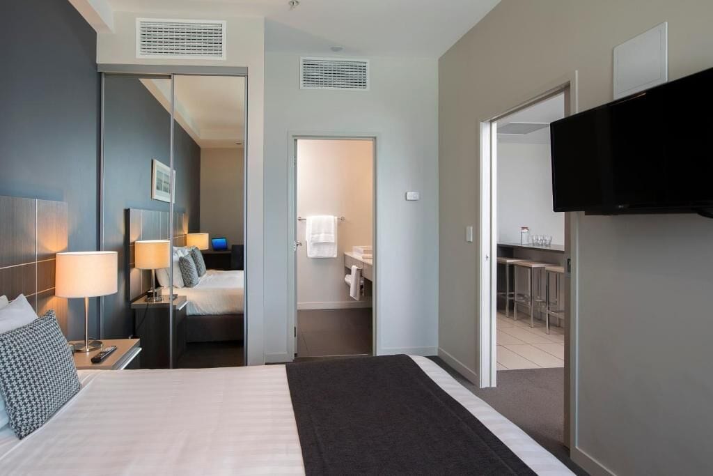 Camera d'albergo con un letto, lampade sui comodini, televisione, bagno con portasciuga e angolo cottura.