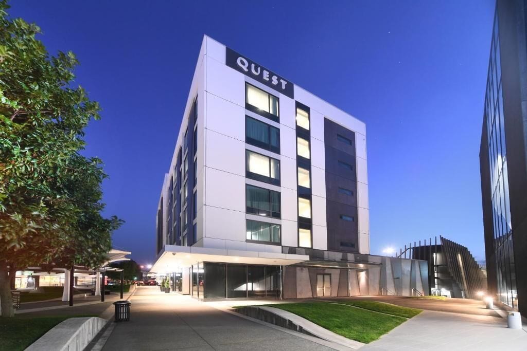 Un hotel moderno con fachada plana, ventanas amplias y un llamativo letrero con el nombre "QUEST".