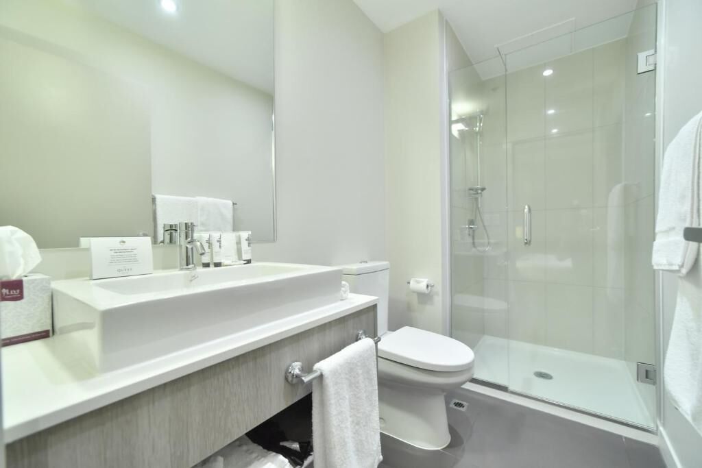 A modern bathroom with a large mirror, a white sink, a toilet, and a glass-enclosed shower.