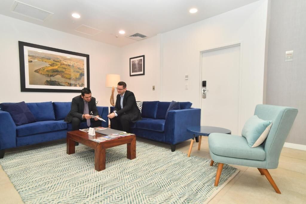 A modern hotel room with a blue sofa set, a wooden coffee table, and a light blue armchair.