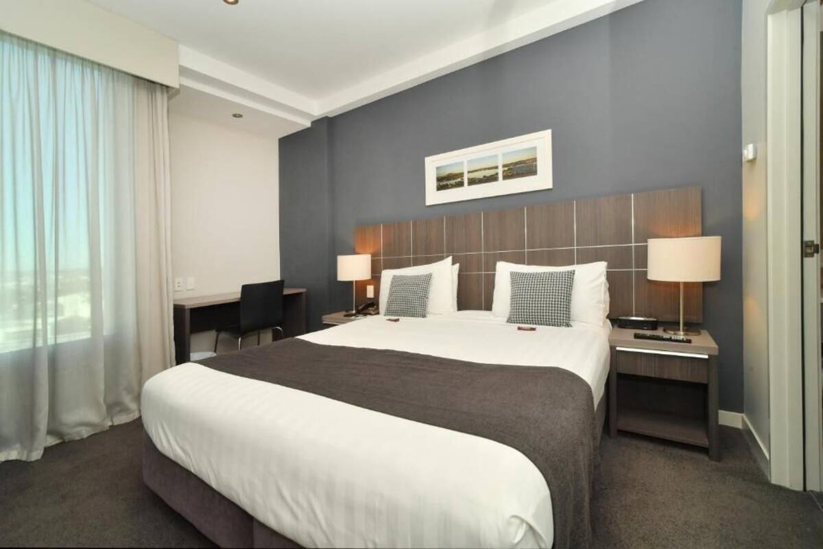 Una habitación de hotel con una cama grande, dos mesitas de noche con lámparas, un escritorio y una silla.