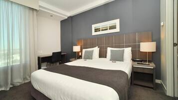 Quarto de hotel com uma cama grande, duas mesas de cabeceira com abajures, uma escrivaninha e uma cadeira.
