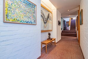 A hallway with white brick walls, a wooden bench, and artwork.