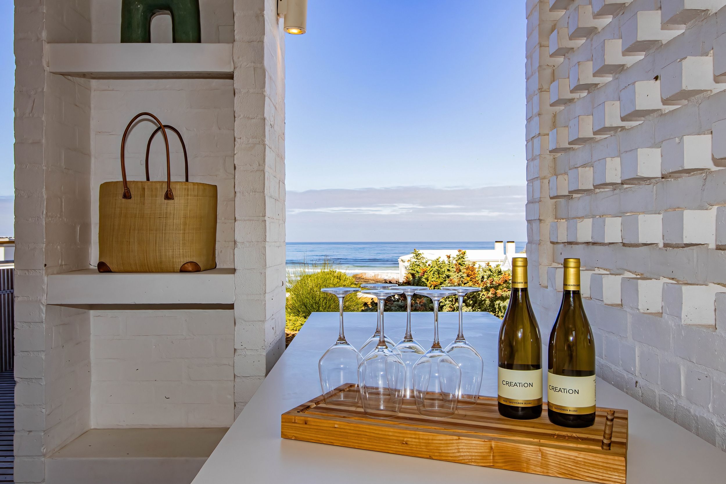 A table with wine bottles and glasses, a wooden tray, and a view of the ocean.