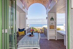 A balcony with a view of the sea, a table with a patterned tablecloth, and a shelf with decorative items.
