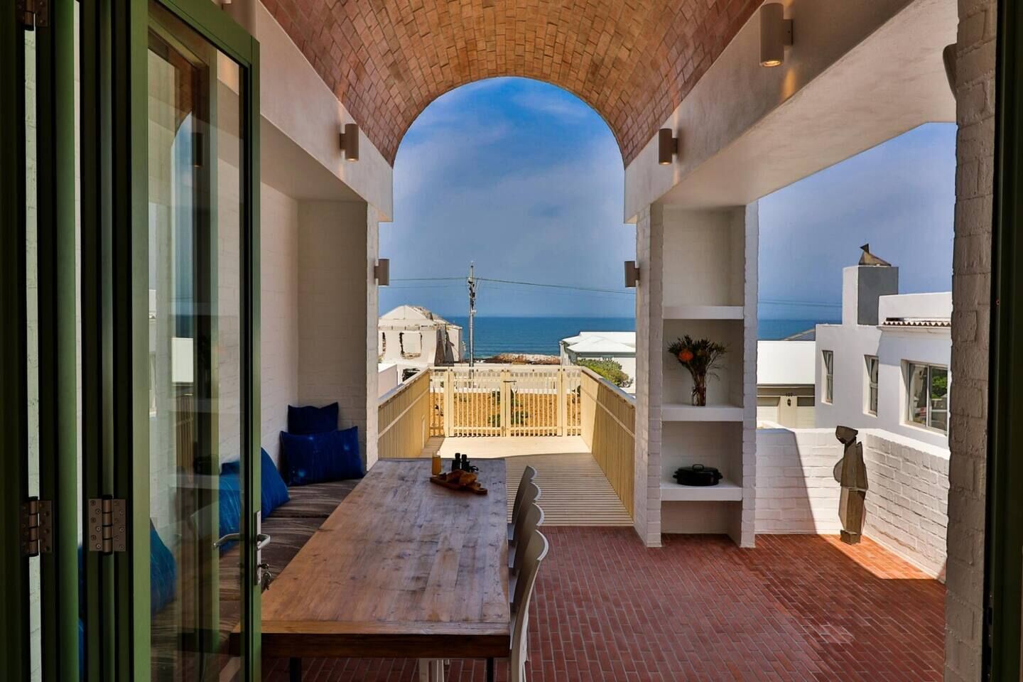 An outdoor patio with a wooden table, seating, and a view of the sea.