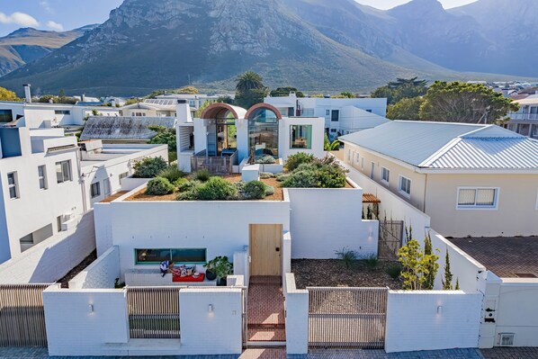 A modern residential area with white buildings, a central structure with a glass facade, and a mountainous backdrop.