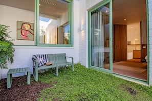 A modern house with a green bench, a small garden, and a large sliding glass door leading to an interior space.