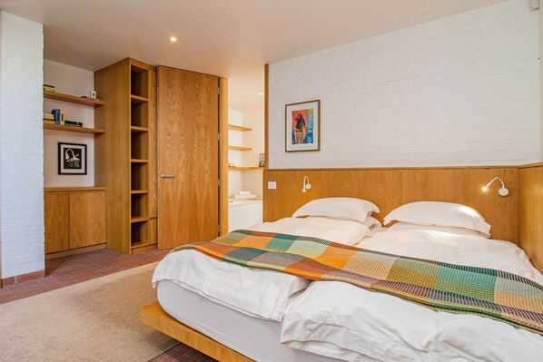 A bedroom with a bed, a wooden wardrobe, a shelf with books, and a framed picture on the wall.