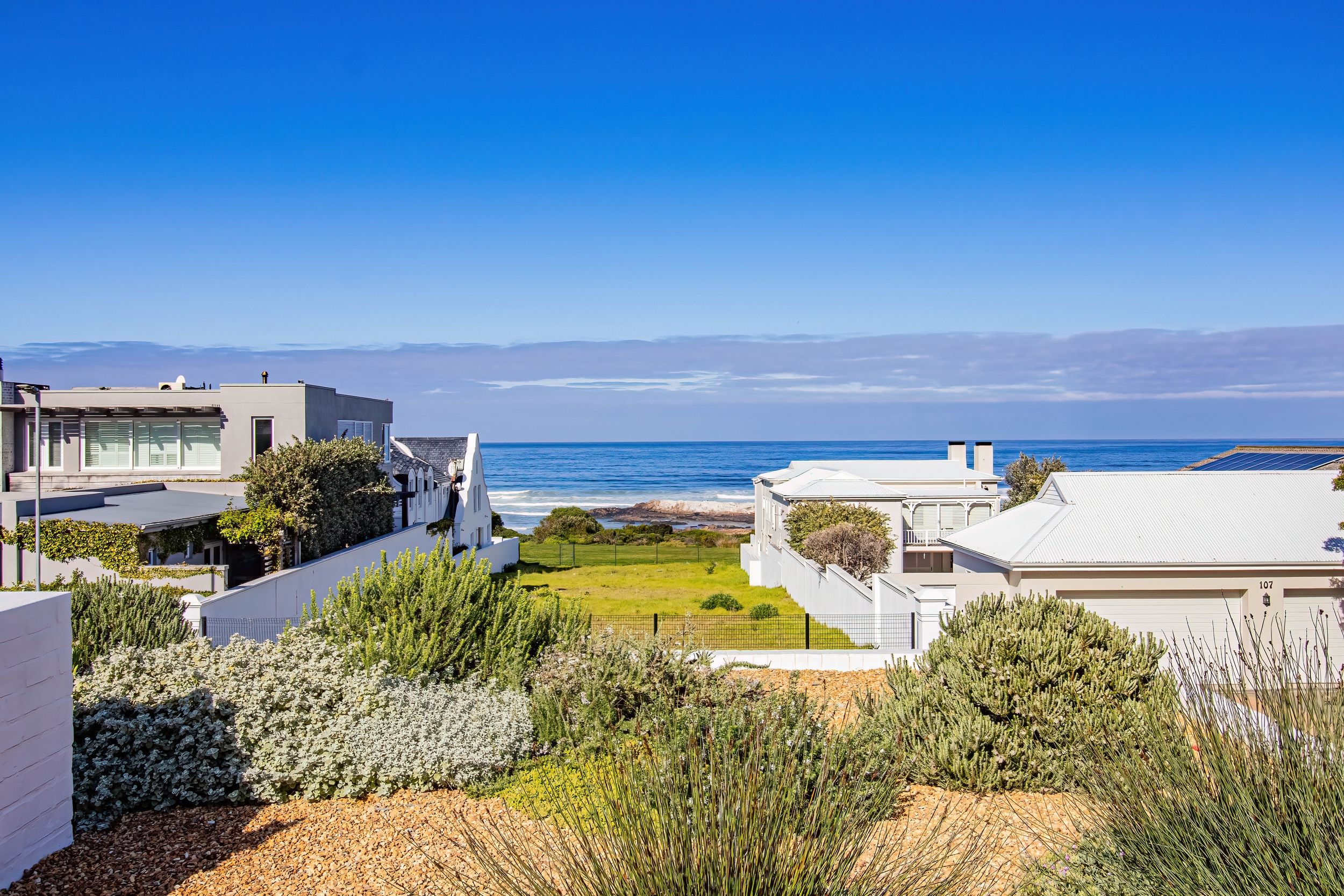 Un quartier résidentiel situé sur la côte, avec des maisons modernes, une vue dégagée sur l’océan et un jardin bien entretenu.