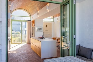 A modern kitchen with an island, a dining area with a table and chairs, and a view through a glass door to an outdoor balcony.
