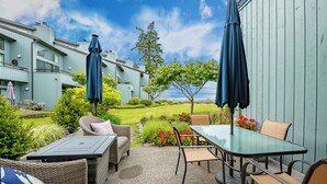 An outdoor patio with wicker furniture, a glass table, and two umbrellas. - The Beach Retreat-Stylish 2-bedroom view condo in Birch Bay  (Blaine)