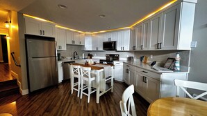 A modern kitchen with white cabinets, a stainless steel refrigerator, a microwave, and a wooden dining table with chairs. - The Beach Retreat-Stylish 2-bedroom view condo in Birch Bay  (Blaine)