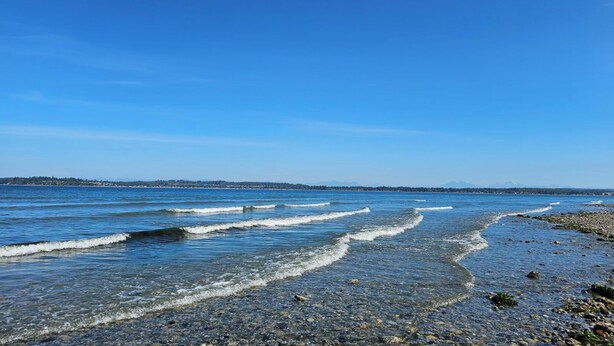 A beach with clear blue water, waves, and a distant mountain range. - The Beach Retreat-Stylish 2-bedroom view condo in Birch Bay  (Blaine)