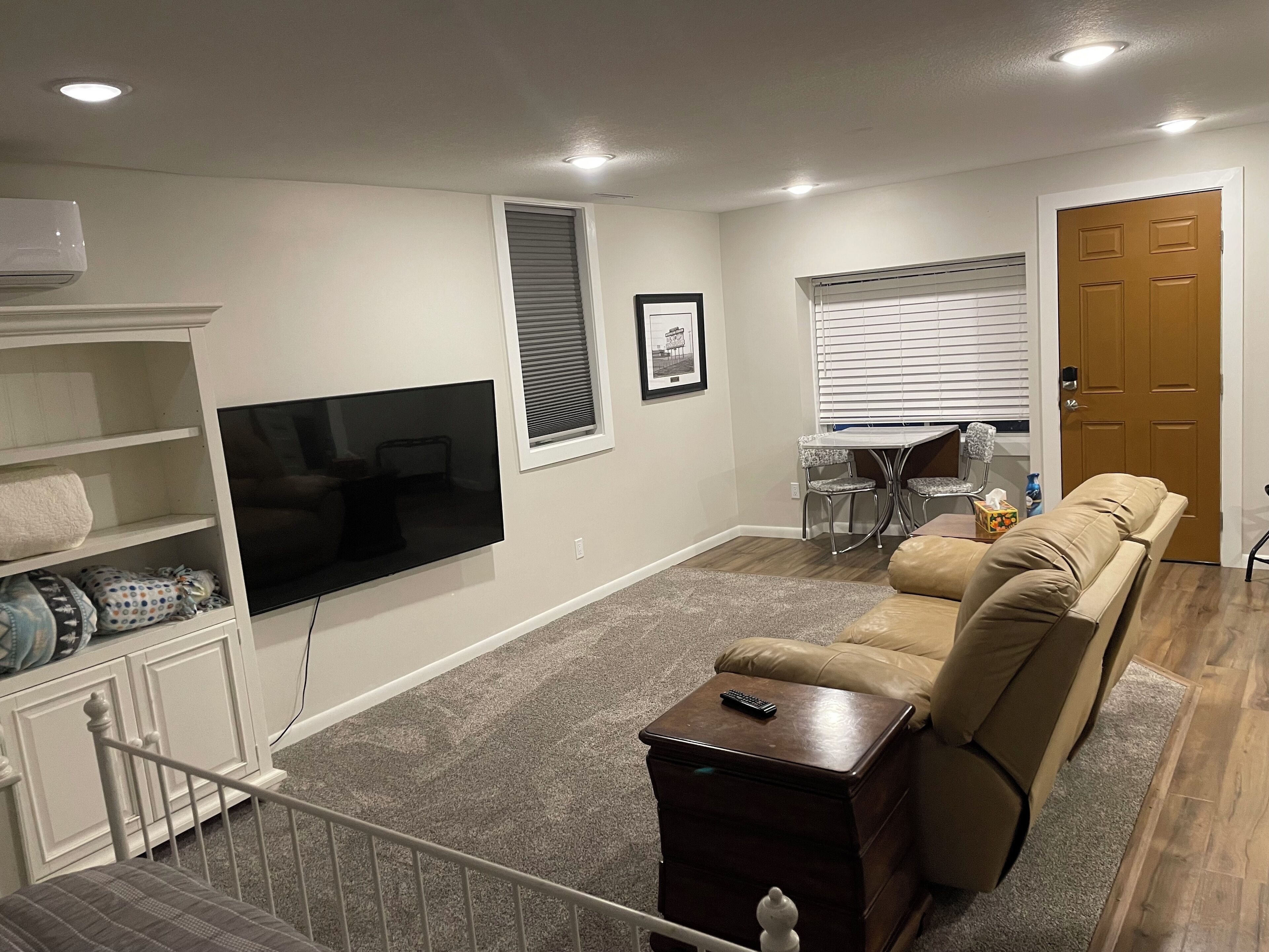 A living room with a TV, a sofa, a dining table with chairs, and a door.